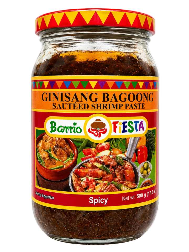 A glass jar of Barrio Fiesta Ginisang Bagoong (spicy sautéed shrimp paste) on a white background. The jar has a red lid with yellow and red patterns, and the label features orange, red, and green sections with product imagery and text.