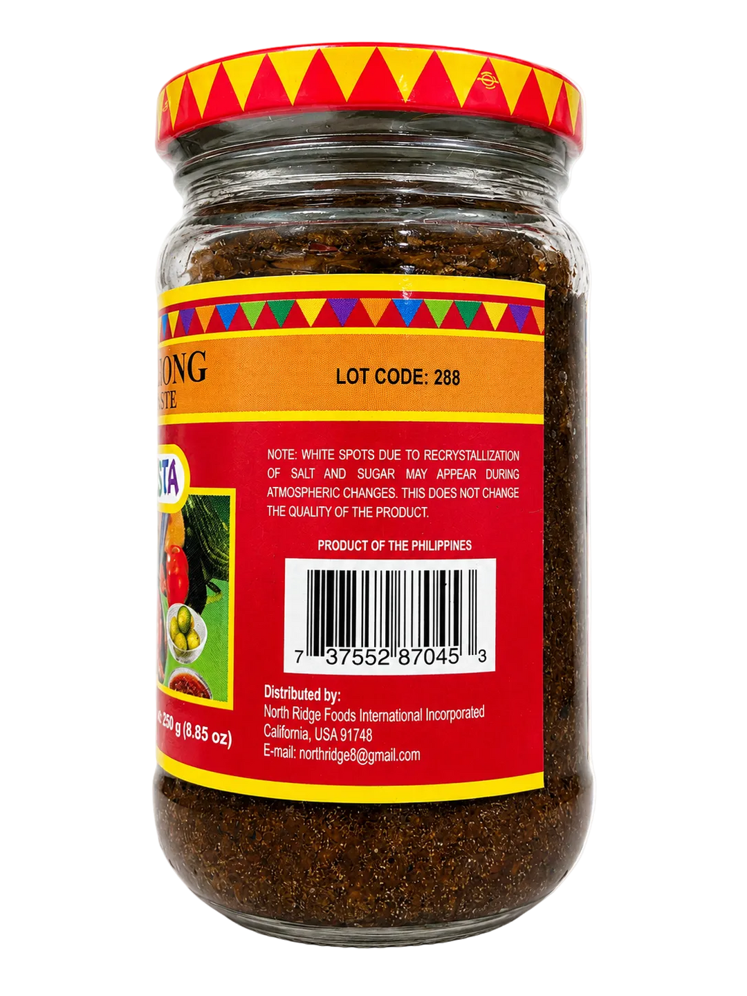 A glass jar of food product with a red and yellow patterned lid and a red label, photographed on a plain white background. The label includes text such as lot code 288 and product details, but the brand name is not clearly legible.