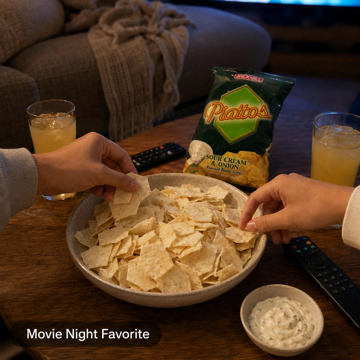 Two hands reaching for Piattos Sour Cream & Onion crisps in a bowl during movie night, with drinks and dip nearby