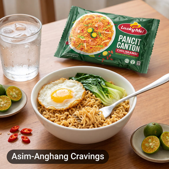A bowl of Lucky Me! Pancit Canton chili-mans noodles with a fried egg, bok choy, and a spoon, shown on a wooden table with the green product packaging, a glass of water, lime halves, and chili slices. Text at the bottom reads 'Asim-Anghang Cravings'.